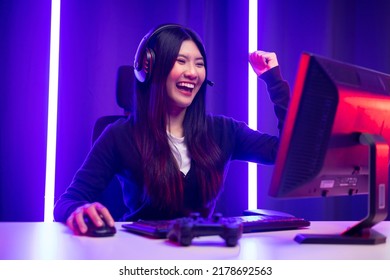 Professional gamer. Young asian pretty woman sitting on chair with computer pc in living room. Happy female Professional Streamer chinese wearing headphone playing game online in dark room neon light - Shutterstock ID 2178692563