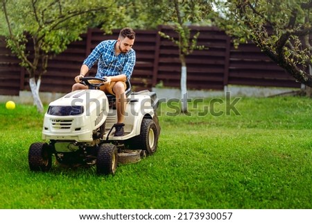 Professional gardener and lawn mower cuts the grass using tractor. Industrial landscaping works