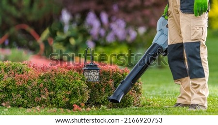 Professional Gardener with Leaf Blower in His Hand Cleaning Residential Backyard Garden. Gardening and Landscaping Industry Theme.