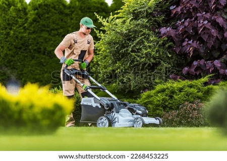Professional Gardener Mowing the Lawn with Cordless Battery Powered Electric Mower. Residential Garden Maintenance Theme. 商業照片 © 