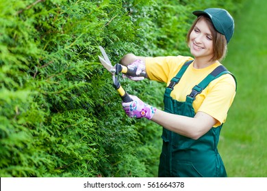 Professional Gardener At Work. Smiling Young Woman Gardener Working With Hedge Shear In The Yard. Garden Worker Trimming Plants. Topiary Art. Gardening Service And Business Concept