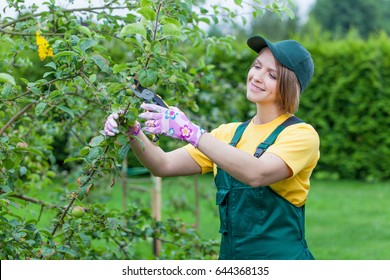 Professional Gardener At Work. Smiling Young Woman Pruning Apple Tree In The Yard. Garden Worker Trimming Plants. Gardening Service, Horticulture And Business Concept