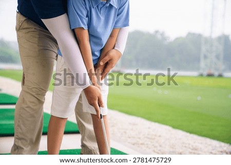 Professional golf instructor demonstrates the grip technique to young student. Focus on proper hand placement and grip helps build strong foundation for future golf success at driving range facility.