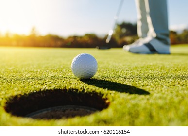 Professional golfer putting ball into the hole. Golf ball by the edge of hole with player in background on a sunny day. - Shutterstock ID 620116154