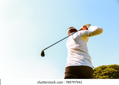 The Professional Golfer Is Swinging Golf Club Overhead Before The Asian Golfer Hits The Ball. He Loves To Play Golf. Senior Golfer Is Playing Golf On A Green With Nice Sky Background And Copy Space