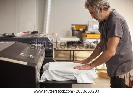 Professional graphic print technician work on digital t-shirt printing machine printer in printing production shop