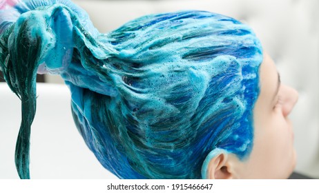 Professional hairdresser holds client's long blue hair in hand while washing hair after process of dyeing hair in beautiful dark blue color. - Powered by Shutterstock