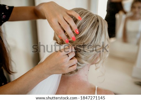 Professional hairdresser makes wedding hairstyle to young beautiful blonde bride on the wedding day. The beautiful bride is almost ready to meet the groom. Free space for text