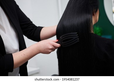 Professional Hairdresser Making Hairstyling For Female Client, Brushing Her Black Shiny Hair. Close-up Picture Of Work Process In Barber Shop. Young Brunette Woman Getting Ready For Party