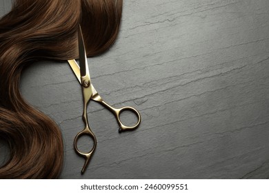 Professional hairdresser scissors with brown hair strand on dark grey table, top view. Space for text - Powered by Shutterstock