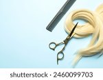 Professional hairdresser scissors and comb with blonde hair strand on light blue background, flat lay. Space for text