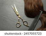 Professional hairdresser scissors and comb with brown hair strand on dark grey table, top view