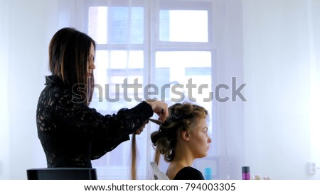 Professional hairdresser, stylist combing hair of female client, using spray and making curls. Beauty and haircare concept