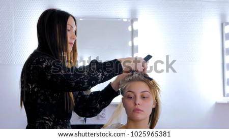 Professional hairdresser, stylist doing hairstyle and using straightener on beautiful long hair of client in white make up room. Beauty and haircare concept