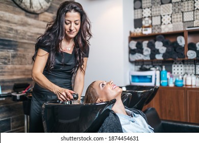 Professional hairdresser washing hair of a beautiful middle-aged woman in hair salon. - Powered by Shutterstock