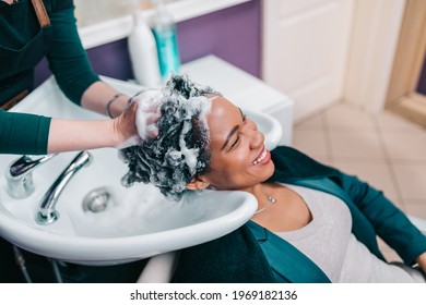 Professional Hairdresser Washing Hair Of A Middle Aged African American Woman In Hair Salon. 