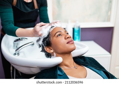 Professional Hairdresser Washing Hair Of A Middle Aged African American Woman In Hair Salon. 