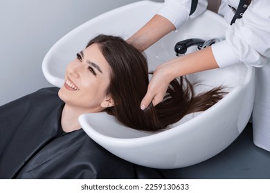 Professional hairdresser washing hair of young woman in beauty salon.The European brunette relaxes at the barber shop. - Shutterstock ID 2259130633