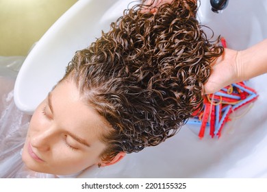 Professional hairstylist washes client’s hair with conditioner shampoo for washing after curling hair. Close up of curlers in hair. Creating hairstyles by a hairdresser in the salon. Shallow depth - Shutterstock ID 2201155325