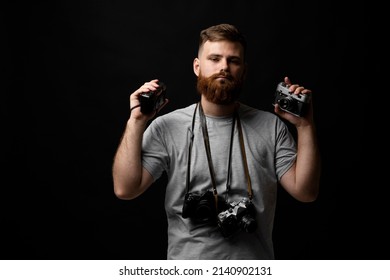 Professional handsome bearded male photographer with bunch of vintage photo cameras in photo studio, isolated on black background.