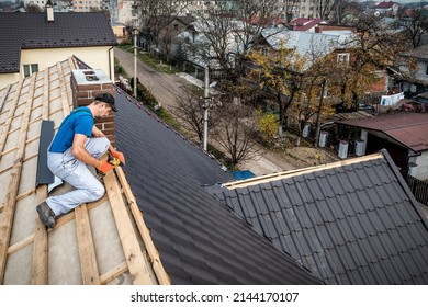 a professional handyman master (roofer) with electric screwdriver covers repairs the roof - Shutterstock ID 2144170107