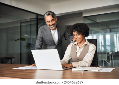 Professional happy busy male business man manager explaining corporate software helping young female employee at work looking at laptop. Busy diverse colleagues working together talking in office. - Powered by Shutterstock