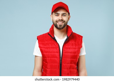 Professional happy delivery guy employee man in red cap white T-shirt vest uniform workwear work as dealer courier look camera isolated on pastel blue color background studio portrait. Service concept