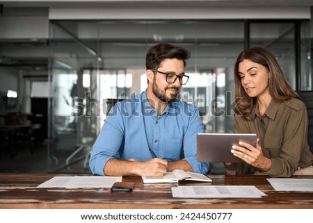 Professional happy manager showing work plan using tab helping employee. Busy colleagues working with digital tablet talking in office. Smiling professional partners having conversation at meeting.