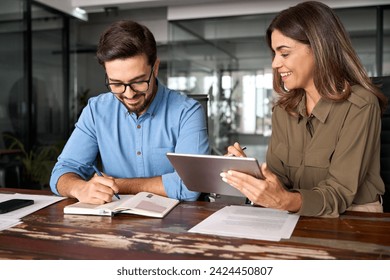 Professional happy middle aged business woman manager explaining work strategy teaching young employee writing notes at workplace. Busy colleagues using digital tablet talking in office. - Powered by Shutterstock