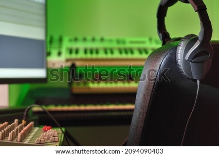 Professional headphones in a music recording studio against a background of blurry synthesizers and electronic musical instruments. Recording studio, workplace of sound engineer and producer.