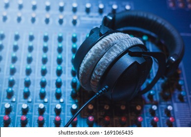 Professional Headphones On A Blue Mixer, Sound Table Or Audio Table And Neon Disco Lights. DJ Booth, Recording Studio For Sound Technician, Music Producer, Musician Or Singer.