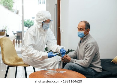 Professional Health Care Doctor In Ppe Suit, Face Mask, Face Shield Preparing The Antigen Test Kit. A Senior Adult Patient Waiting At Home To Take Nasal Culture Sampling While Coronavirus Pandemic.