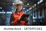 Professional Heavy Industry Engineer Worker Wearing Safety Uniform and Hard Hat Uses Tablet Computer. Serious Successful Female Industrial Specialist Walking in a Metal Manufacture Warehouse.