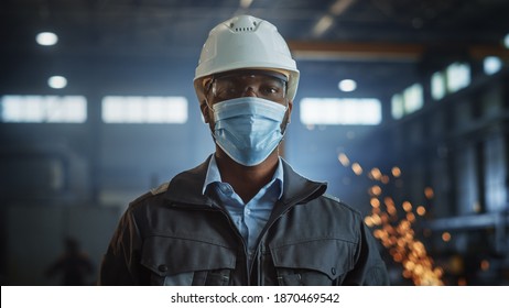 Professional Heavy Industry Engineer Worker Wearing Safety Face Mask, Uniform, Glasses and Hard Hat in a Steel Factory. African American Industrial Specialist Standing in Metal Construction Facility.