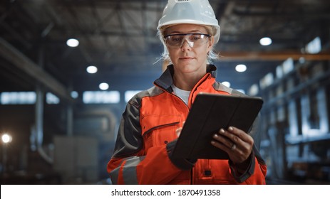 Professional Heavy Industry Engineer Worker Wearing Safety Uniform and Hard Hat Uses Tablet Computer. Serious Successful Female Industrial Specialist Walking in a Metal Manufacture Warehouse. - Powered by Shutterstock