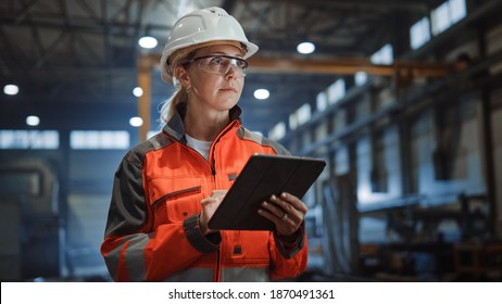 Professional Heavy Industry Engineer Worker Wearing Safety Uniform and Hard Hat Uses Tablet Computer. Serious Successful Female Industrial Specialist Walking in a Metal Manufacture Warehouse. - Shutterstock ID 1870491361