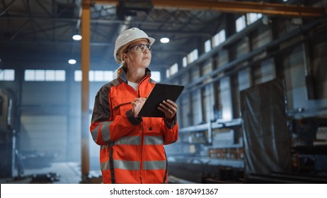 Professional Heavy Industry Engineer Worker Wearing Safety Uniform and Hard Hat, Using Tablet Computer. Serious Successful Female Industrial Specialist Walking in a Metal Manufacture Warehouse. - Powered by Shutterstock