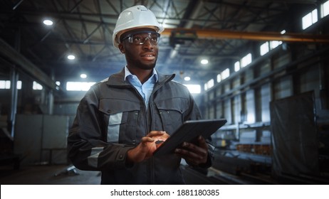 Professional Heavy Industry Engineer Worker Wearing Safety Uniform and Hard Hat Uses Tablet Computer. Smiling African American Industrial Specialist Walking in a Metal Construction Manufacture.