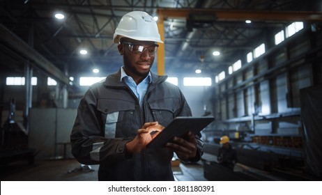 Professional Heavy Industry Engineer Worker Wearing Safety Uniform And Hard Hat Uses Tablet Computer. Smiling African American Industrial Specialist Walking In A Metal Construction Manufacture.