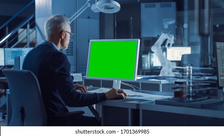 Professional Heavy Industry Engineer Works On Green Mock-up Screen Computer. Engineering Bureau And Industrial Design Agency With Various Robotic, Architectural And Machinery Components