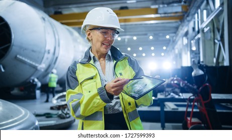 Professional Heavy Industry Female Engineer Wearing Safety Uniform, Holds Digital Tablet Computer And Explains Product Design. Industrial Factory Construction Of Oil, Gas And Fuels Transport Pipeline