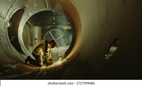 Professional Heavy Industry Welder Working Inside Pipe, Wears Helmet And Starts Welding. Construction Of The Oil, Natural Gas And Fuels Transport Pipeline. Shot With Warm Light.