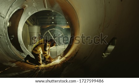 Professional Heavy Industry Welder Working Inside Pipe, Wears Helmet and Starts Welding. Construction of the Oil, Natural Gas and Fuels Transport Pipeline. Shot with Warm Light.
