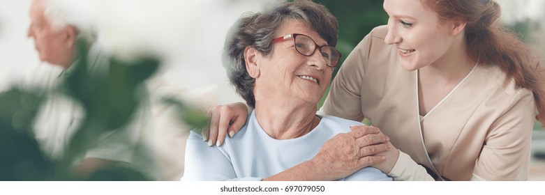 Prestador de cuidados profesional que reconforta a una mujer mayor sonriente en el hogar de ancianos