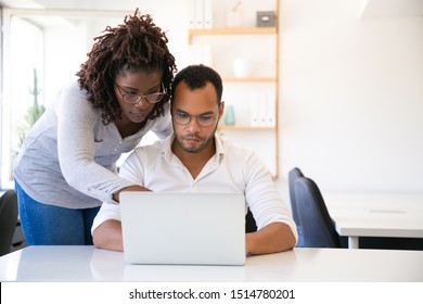 Professional Helping New Employee With Report. Business Man And Woman In Casual Sitting And Standing At Workplace, Using Laptop, Pointing At Screen. Mentorship Concept