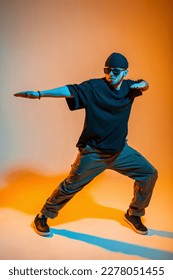 Professional hip hop dancer man in fashion clothes with a hat, sunglasses, t-shirt and sneakers dances in a color studio with orange and neon lights - Shutterstock ID 2278051455