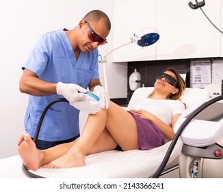 Professional Hispanic Male Cosmetologist Performing Laser Hair Removal For Young Female Patient In Clinic Of Esthetic Cosmetology