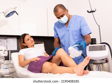 Professional Hispanic Male Cosmetologist Performing Laser Hair Removal For Young Female Patient In Clinic Of Esthetic Cosmetology