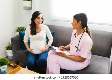 Professional hispanic midwife in a uniform scrub speaking to a happy caucasian pregnant woman and taking notes about her symptoms and health