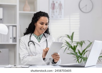 Professional Hispanic woman doctor sitting in a clinic office, smiling as she reviews patient data on a digital tablet. Modern healthcare setting. - Powered by Shutterstock